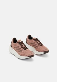 Baskets de sport rose clair avec tige en mesh, accents bruns, semelle blanche rembourrée et design à lacets. Détails texturés pour la respirabilité et le soutien.