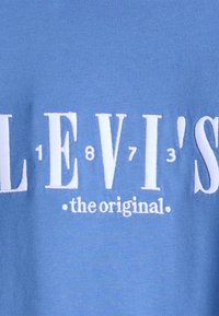 Mėlyna medvilninė marškinė su baltais siuviniais tekstu "LEVI'S 1873 originalas". Lygi tekstūra su laisvu siluetu.