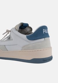 Sneaker in pelle bianca con accenti in suede beige, cappuccio del tallone in tessuto blu, suola spessa color crema e "You Can Smile" impresso sulla suola.