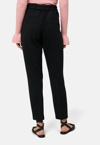 Czarne, dopasowane spodnie z wysokim stanem, płaskim przodem i dwiema kieszeniami z tyłu. Połączone z czarnymi, płaskimi sandałami z krzyżującymi się paskami.