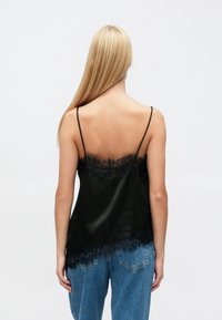 Zwarte satijnen cami-top met verstelbare bandjes, voorzien van een kanten rand langs de halslijn en zoom. Ontworpen met een losse pasvorm voor comfort.