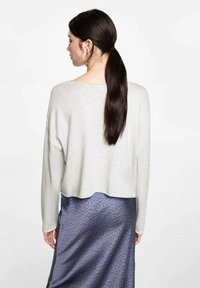 Vaaleanharmaa lyhyt villapaita, joka on valmistettu pehmeästä materiaalista, yhdistettynä tummiin painettuihin hameeseen, jossa on hienovarainen kuvio.