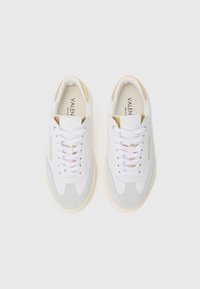 Sneaker bianchi e grigio chiaro realizzati in materiali scamosciati e in pelle. Presentano lacci piatti, un interno imbottito e dettagli in tonalità oro sul tallone.
