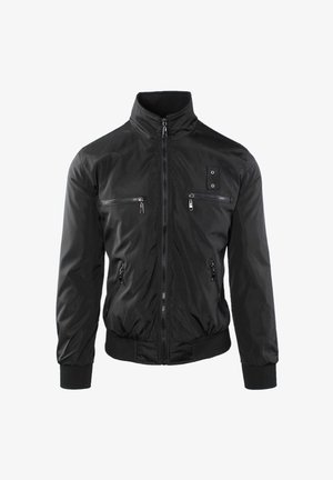 Giacca nera leggera con collo alto, quattro tasche frontali con cerniera, polsini e orlo a costine, e una piccola toppa con due occhielli metallici.