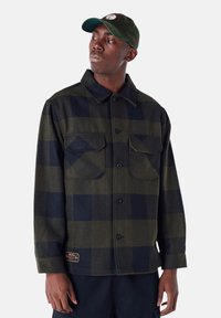 Groene en zwarte geblokte flanellen shirt met knoopsluiting, twee borstzakken en een geweven label aan de linksonderkant. Katoenen materiaal.