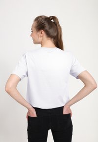 Hvid bomulds t-shirt med korte ærmer, let afslappet pasform, set fra ryggen, parret med sorte jeans. Glat tekstur, minimalistisk design.