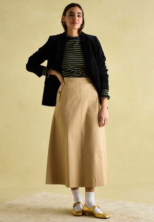 Black corduroy blazer, striped green and yellow top, beige long skirt, white socks, and gold Mary Jane shoes with a side button detail.