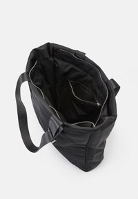Saco tote preto com um acabamento suave e mate. Apresenta um fecho com zíper, alças robustas e um bolso interior para organização. Textura suave.
