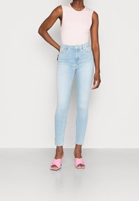 Vaqueros de tiro alto en azul claro con corte ajustado y un ligero desvanecido, combinados con una blusa sin mangas de rayas en rosa y sandalias rosas tipo slide.