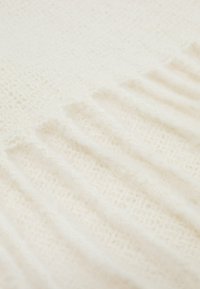 Kudotun kermaisen värinen kangas, jossa on pehmeä, teksturoitu pinta, joka esittelee ribbikuvioita ja hienovaraisia paksuusvaihteluja.