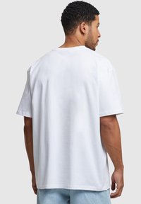 Hvid oversized bomulds t-shirt med rund halsudskæring og korte ærmer, der har en glat tekstur og lige kant, set fra bagsiden.