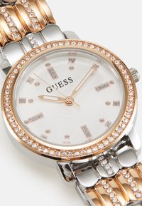 Silberne und roségoldene Uhr mit einem strukturierten weißen Zifferblatt, Kristallakzenten und einem verlinkten Armband. Sie hat ein rundes Gehäuse und rechteckige Stundenmarkierungen.