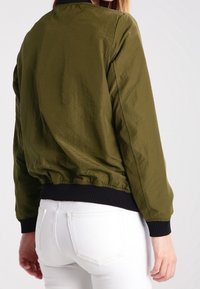 Olijfgroene bomberjack van lichtgewicht stof, met een zwarte geribbelde kraag en manchetten, elastische zoom en een gladde textuur.