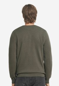 Olivgrön stickad tröja med rund halsringning, långa ärmar och ribbade mudd och fåll. Slät textur med en figurnära silhuett.