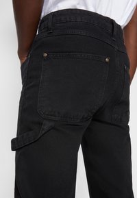 Czarne spodnie dżinsowe z wysokim stanem, dwoma tylnymi kieszeniami z metalowymi nitami oraz bocznym paskiem jako dodatkowy detal. Gładka tekstura i dopasowany krój.