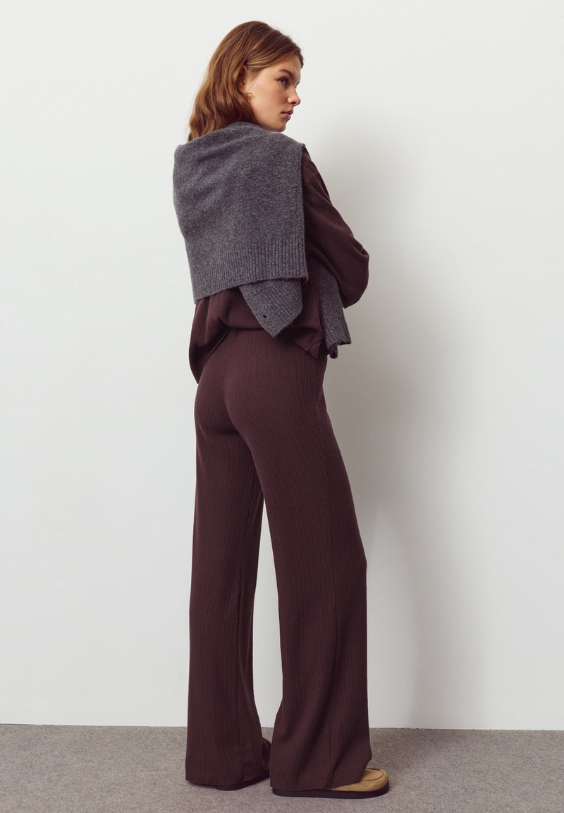 Pull en tricot gris posé sur un haut côtelé marron foncé et un pantalon taille haute assorti. Texture douce avec des jambes larges, associé à des chaussures beiges.