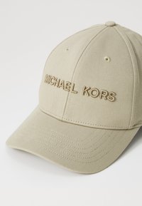 Beige puuvillane beisbolimüts kumerate äärega. Esiküljel on sama värvi reljeefne "MICHAEL KORS" tekst. Tavaline kuue paneeli disain.