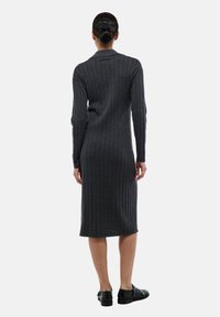 Robe midi en tricot côtelé gris foncé avec des manches longues et une silhouette ajustée. Présente un col rond et une texture subtile. Portée avec des chaussures noires.