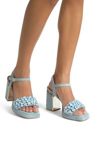 Sandali platform blu cielo con tacco a blocco spesso, caratterizzati da un upper decorato con gemme e una cinghia alla caviglia regolabile. Texture liscia con dettagli decorativi.