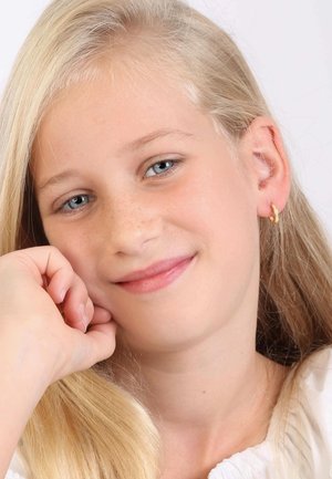Meisje met lang blond haar, lichte huid, die een simpele gouden ringoorbel draagt. Ze steunt met haar kin op haar hand en glimlacht zachte.