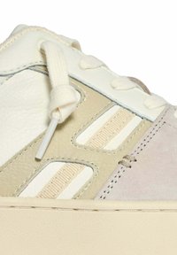 Sneaker met een witte leren bovenkant, beige accenten, textuur overlays en beige veters. Bevat een crème rubberen zool en stikdetails.