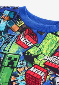 Blaues Sweatshirt mit Minecraft-Themenmotiven, darunter TNT-Blöcke und Charaktere, auf einem lebendigen, mehrfarbigen Hintergrund mit verschiedenen Mustern.