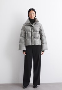 Pufferjakke i skinnende grå med en kort design, oversized ermer og høy krage. Kombinert med svarte, vide bukser.