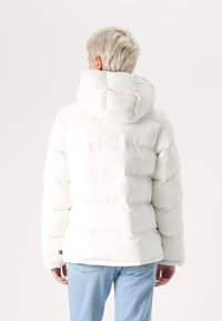 White puffer jacket with a hood, featuring quilted sections and a smooth texture. Paired with light blue denim jeans.