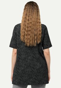 Top corto negro de manga corta con un patrón floral texturizado. La vista trasera muestra un corte relajado y un escote redondo, confeccionado con tela ligera.