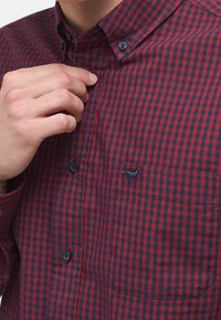 Camisa de botones con estampado a cuadros rojos y azul marino, de tela de algodón, con botones y un bolsillo con un pequeño detalle de logo bordado.