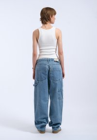 White ribbed tank top with a fitted shape paired with loose, light blue denim cargo pants featuring multiple pockets and a relaxed fit.