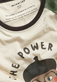 Kermankoska t-paita, jossa on vihreät lyhyet hihat, musta urheilureuna kaula-aukossa. Paitassa on sarjakuvamainen kasvokuva ja teksti "TEHO" mustalla.