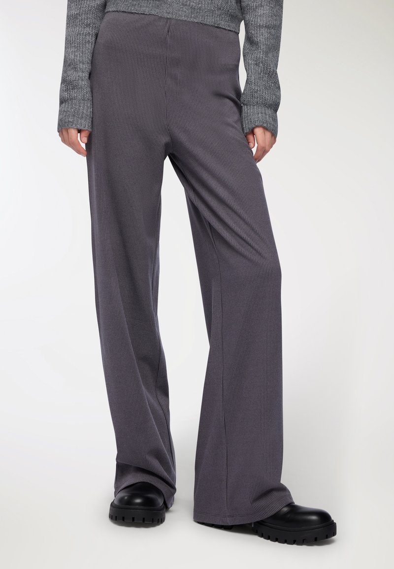 Spodnie szerokie w ciemnoszary wzór w prążki. Wykonane z miękkiego materiału, charakteryzujące się luźnym krojem i gładką, swobodnie układającą się fakturą.