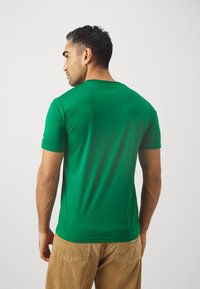 Zöld rövid ujjú póló kerek nyakkal, sima anyagból készült, testhez álló fazonban, finom varrási részletekkel.