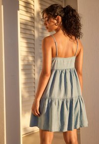 Vaaleansininen hihaton mekko, joka on valmistettu pehmeästä kankaasta, sisältää kerroksellisen muotoilun, jossa on levenevä helma ja säädettävät olkaimet. Rakenteellinen ja viuhtova.