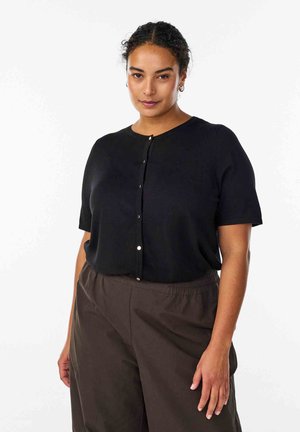 Črni kratek pulover z kratkimi rokavi iz mehke tkanine z okroglim izrezom in okrasnimi gumbi spredaj, združen z ohlapnimi rjavimi hlačami.