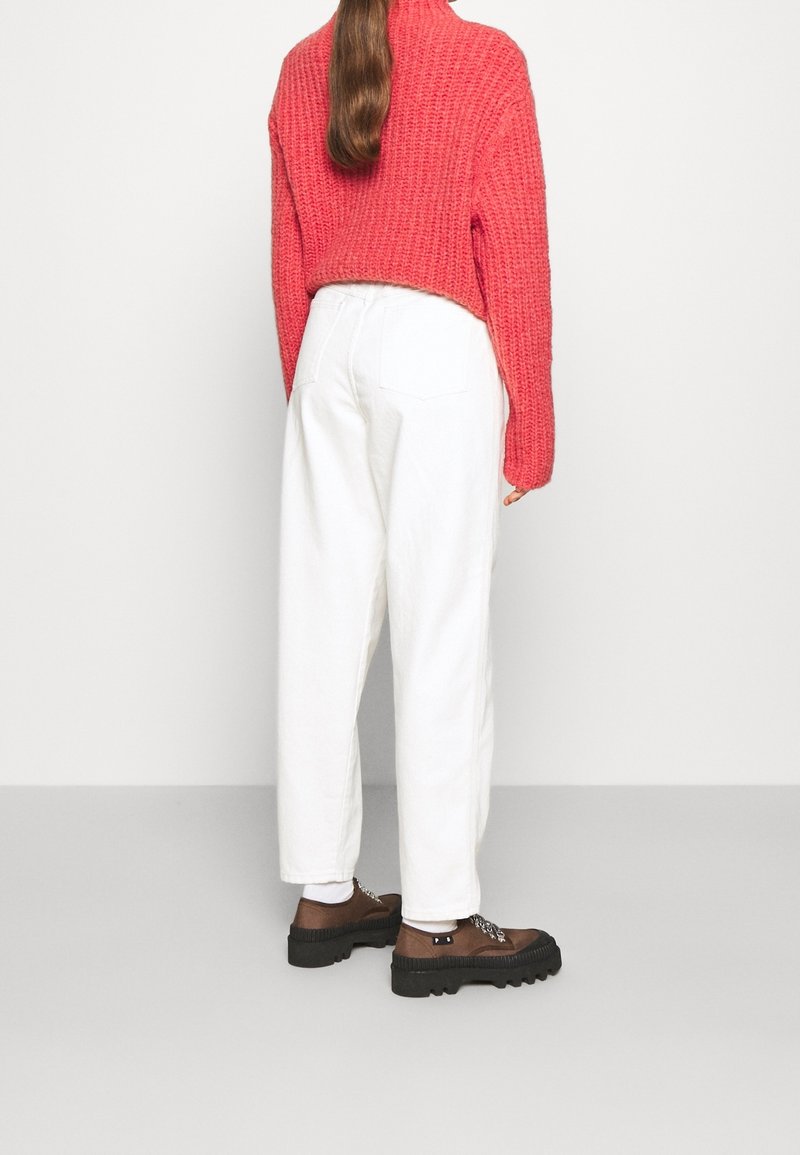 Pull en laine rouge avec un col haut, pantalon blanc à jambes larges et chaussures marron avec des semelles épaisses et des lacets décoratifs.