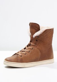 Sneaker montante en cuir marron avec doublure en polaire blanche, lacets beige et semelle en caoutchouc beige avec logo UGG.