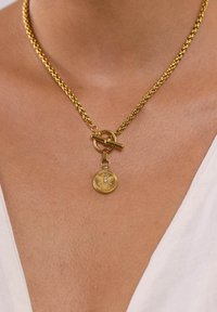 Kette aus vergoldetem Metall mit einem Toggle-Verschluss, ausgestattet mit einem runden Anhänger, der mit einem Bienenmotiv geprägt ist und einem kleinen Strassstein-Akzent.