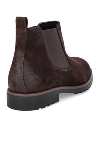 Brązowy zamszowy botek na kostkę z elastycznym panelem bocznym, zaokrąglonym noskiem, teksturowanym wierzchem i czarną gumową podeszwą. Wysokość obcasa jest umiarkowana.