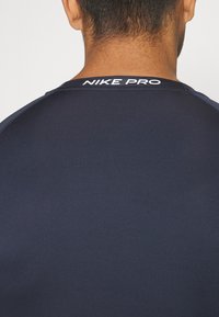 Navy Nike Pro Sportshirt mit Rundhalsausschnitt und glattem, strukturiertem Stoff sowie einem weißen Logodetail am Hinterkragen.