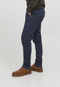 Marineblaue Chinos aus Baumwolle, Slim Fit, mit Fronttaschen und einer Gesäßtasche, kombiniert mit braunen Wildleder Schnürschuhen.