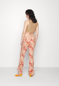 Top cropped castanho em estilo bandagem com costas atadas, combinado com calças com padrão colorido em espirais. Mules amarelas de salto completam o visual.