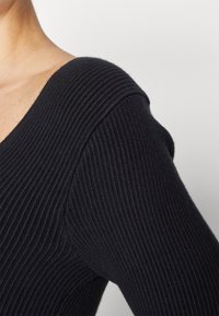 Sort ribstrikket sweater med dyb V-hals og tætsiddende ærmer, der fremhæver tekstur og struktureret design.