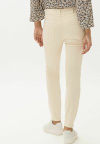 Jeans ajustados de color beige claro con una textura suave, que cuentan con bolsillos traseros y un detalle en el logo, combinados con zapatillas de plataforma blancas.