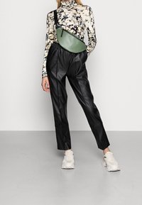 Groene faux leren crossbody tas, zwarte leren high-waisted broek en een gestreepte lange mouwen coltrui, gedragen met lichte sneakers.
