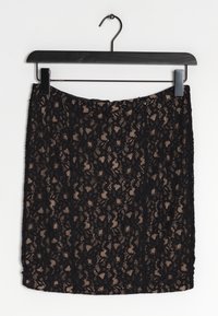 Jupe en dentelle noire suspendue à un cintre, ornée de motifs floraux, d'une texture semi-transparente et d'une coupe ajustée.