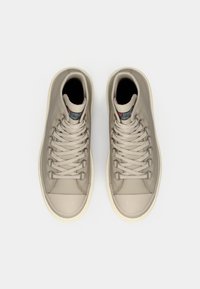 Ein Paar beige High-Top-Sneaker mit dicken weißen Sohlen und Schnürsenkeln, von oben auf einem weißen Hintergrund gezeigt.