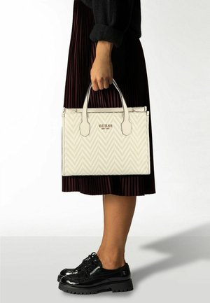 Witte handtas met visgraatpatroon en zwarte accenten, bovenhandvatten en een geperst logo. Gecombineerd met een donkeren geplooide rok en zwarte plateauzolen.