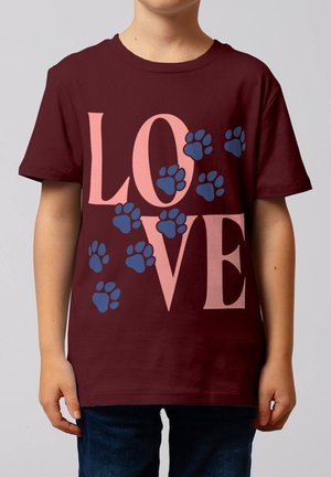Enfant portant un t-shirt rouge foncé avec de grandes lettres roses formant le mot « LOVE » et des empreintes de pattes bleues dispersées sur le devant.